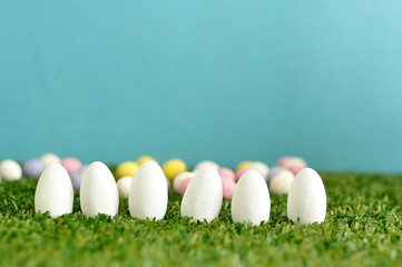 A row of white easter eggs displayed on artificial grass with speckled easter eggs that is out of focus