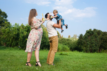 Young attractive family playing with child in a meadow and drinking juice