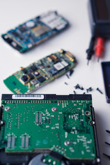 disassembled broken cellphones and hard disk drive on a white desk preparing for repair. focus on...