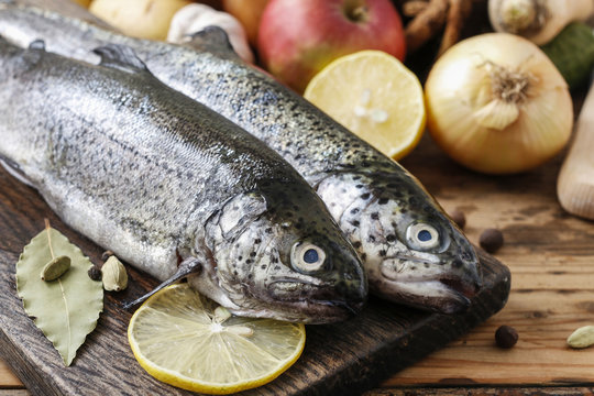 Two rainbow trouts on rustic wooden table among herbs and vegetables