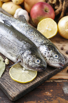 Two rainbow trouts on rustic wooden table among herbs and vegetables