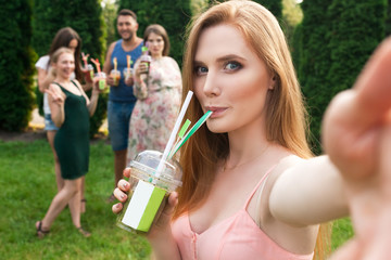 Friends rest and drink juice in the garden, and the girl makes selfie