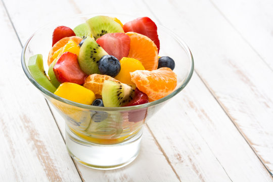 Fruit salad in crystal bowl on white wooden table.
