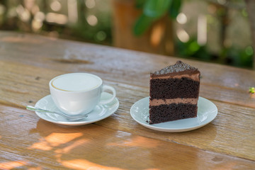 Cup of coffee and piece of chocolate cheesecake on wooden background at yard.