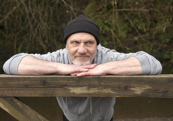 Casual mature man leaning against an old wooden gate outdoors 