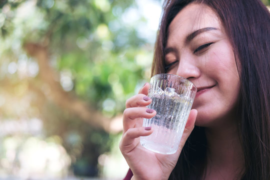 A woman holding and drinking cold water with blur nature background