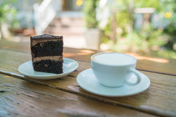 Cup of coffee and piece of chocolate cheesecake on wooden background at yard.