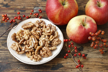 Bowl of walnuts and red apples on wooden table