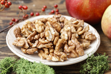 Bowl of walnuts and red apples on wooden table