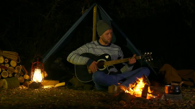 Young  man playing guitar near the bonfire.
