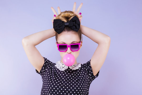 Portrait humoristique d'une jeune femme faisant une bulle de chewing gum les doigts en "V" derri&egrave;re la t&ecirc;te