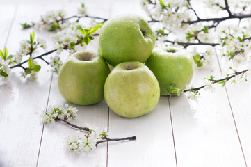 Fototapeta na wymiar Ripe green apples with spring flowers on a white wooden background.