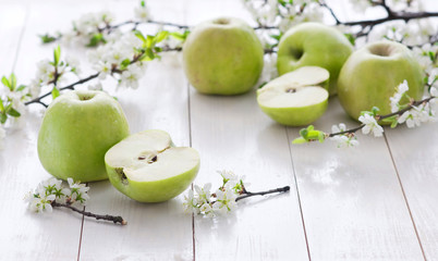 Ripe green apples with spring flowers on a white wooden background.
