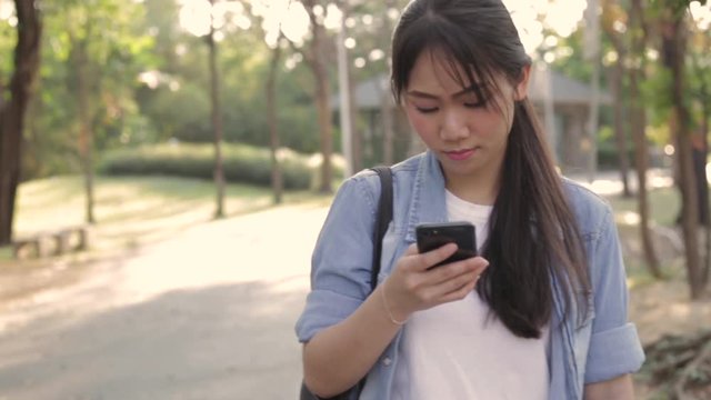 Young asian woman using smart phone while walking in public park on holidays