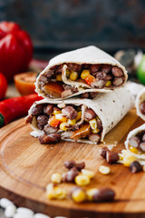 Nice vegetarian burrito over black table on wooden board.