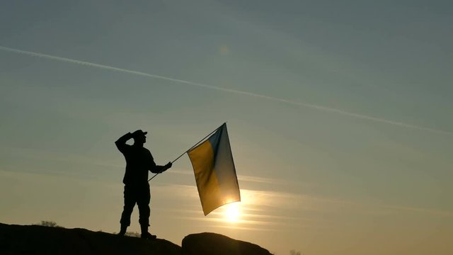 Soldier, patriot saluting and holding flag of Ukraine outdoors.