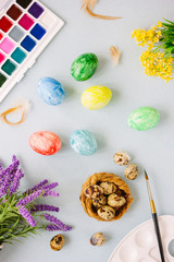 Easter composition - top view of colored eggs, paints, flowers and paint brush.