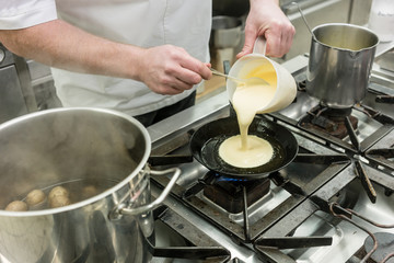 Fototapeta na wymiar Chef preparing pancake dessert pouring dough into pan in kitchen