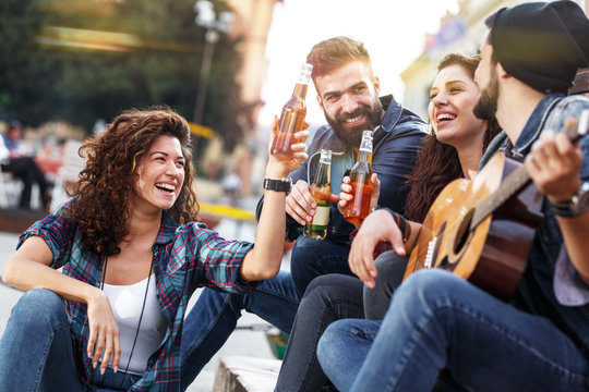 Group of young people hangout  on street in downtown.They standing by the city square,drinking and playing guitar.