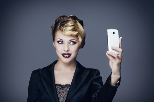 Portrait d'une jeune femme en tailleur,de face, se prenant en photo avec son téléphone portable