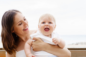 Happy and young mother sitting on a bench and holding her baby. Love and family concept.