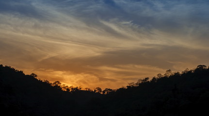 Mountain forest landscape under evening sky with clouds in sunlight and trees silhouettes. Majestic sunset in indian Himalaya mountains near Rishikesh, Uttharakand.