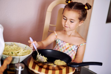 Cute little girl cooking potato pancakes at home