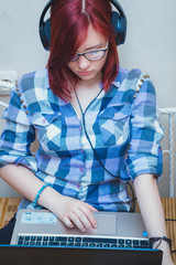 Beautiful young woman with Red Hair with headphones and laptop watching a movie on notebook in bed.