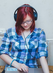 Beautiful young woman with Red Hair with headphones and laptop watching a movie on notebook in bed.