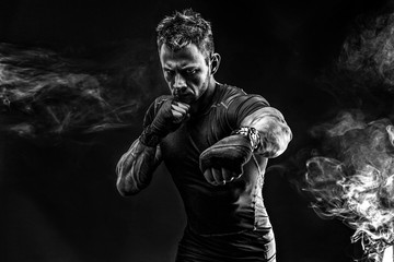 Studio portrait of fighting muscular man in smoke on black background