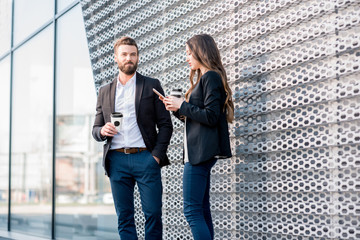 Caucasian business couple standing together outdoors during the coffee break near the modern building facade