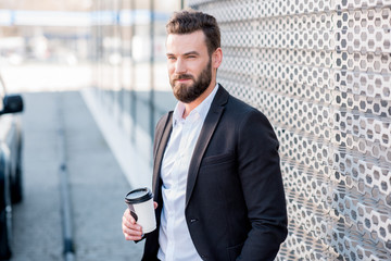 Elegant businessman standing with coffee to go near the car at the modern petrol station