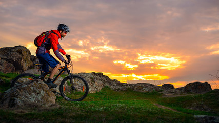 Naklejka premium Cyclist Riding Mountain Bike on the Spring Rocky Trail at Beautiful Sunset. Extreme Sports and Adventure Concept.