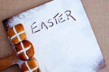 hot cross buns on floured wooden cutting board, with word Easter written in flour
