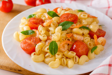 Pasta with shrimps, cherry tomatoes and basil in white plate.