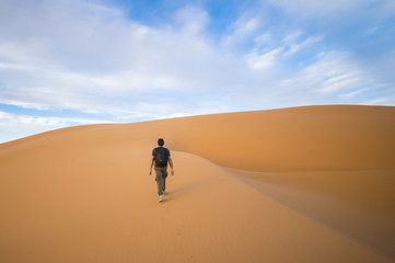 Fototapeta na wymiar A man walks on the dunes in the Sahara Desert at sunset - Merzouga - Morocco