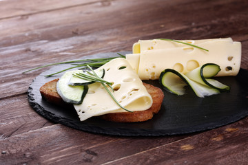 Bread with slices of cheese for lunch table. Sharing antipasti on party or summer picnic time over wooden rustic background.