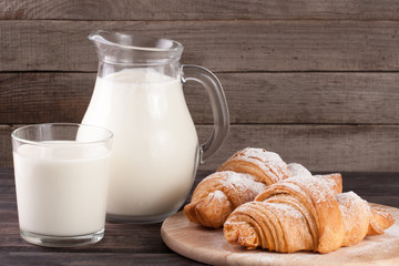 jug and glass of milk with croissants on a wooden background