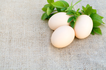 Three fresh chicken eggs and green leaves on a sackcloth tablecloth