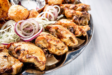 Meat plate with delicious pieces of meat, potatoes, onion and candle on white wooden table