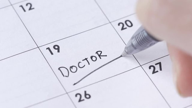 Writing DOCTOR APPOINTMENT on a calendar to remember this date.