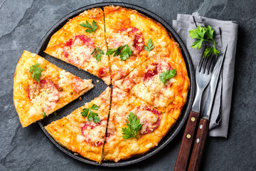 Cut pizza with salami on iron plate on slate background