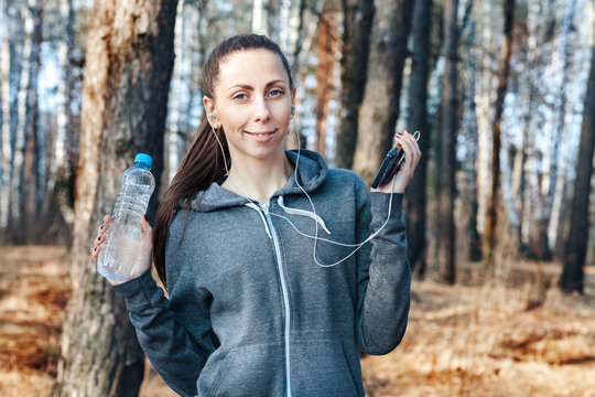 Healthy fitness woman holds a bottle of water and a telephone after running on nature, in the forest