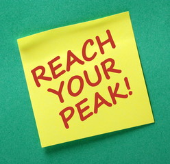 The words Reach Your Peak in red text on a yellow stick note as a reminder to strive for optimum performance