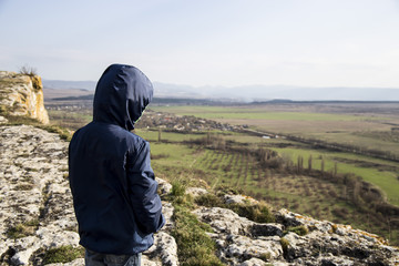 A little boy in a blue jacket is standing on a mountain. White cliff (Ak-Kaya) in the Crimea. Stone blocks and views of the wide steppe. Spring, green grass and clear sky