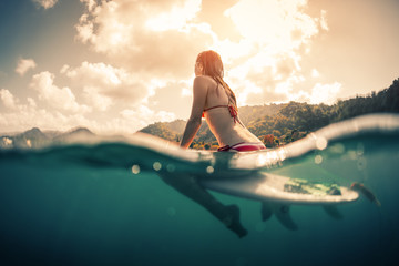 Young woman sitting on surfboard in the ocean. Splitted shot with underwater view - obrazy, fototapety, plakaty