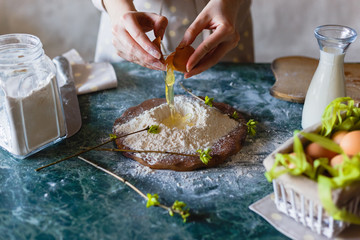 The baker pours the egg into the funnel in the flour on the table.