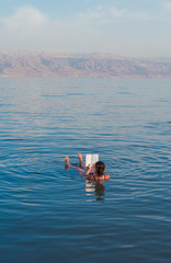 Young woman reads a book floating in the waters of the Dead Sea in Israel
