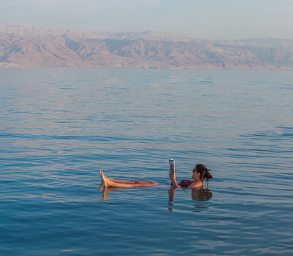 KALIA BEACH, ISRAEL - FEBRUARY 27, 2017:  Young woman reads a book floating in the waters of the Dead Sea in Israel