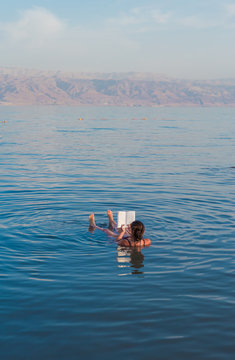 Young woman reads a book floating in the waters of the Dead Sea in Israel